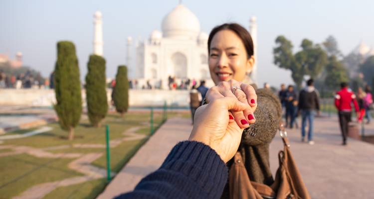 Een voorgrondhand leidt partner naar een zacht wazig Taj Mahal in het ochtendlicht.