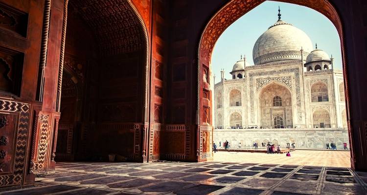 Taj Mahal encadré par une arche avec quelques personnes visibles dans la cour.