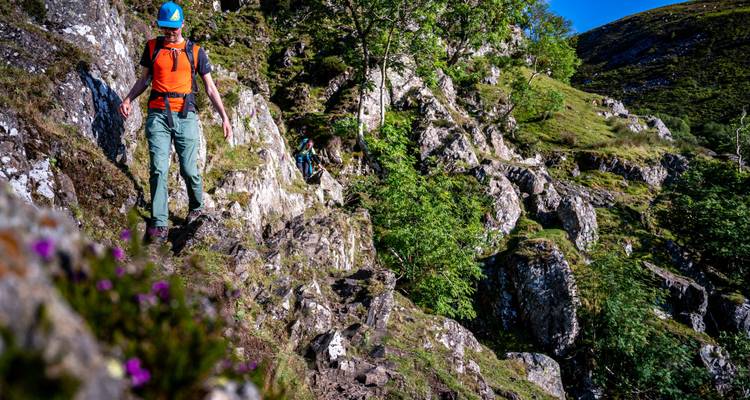 Een persoon die wandelt op rotsachtig terrein met weelderige begroeiing.