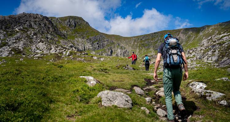 Groep wandelaars op een graspad omringd door heuvels.