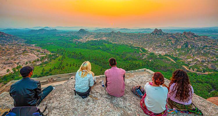 Des gens assis sur une colline regardant le coucher de soleil sur un paysage.