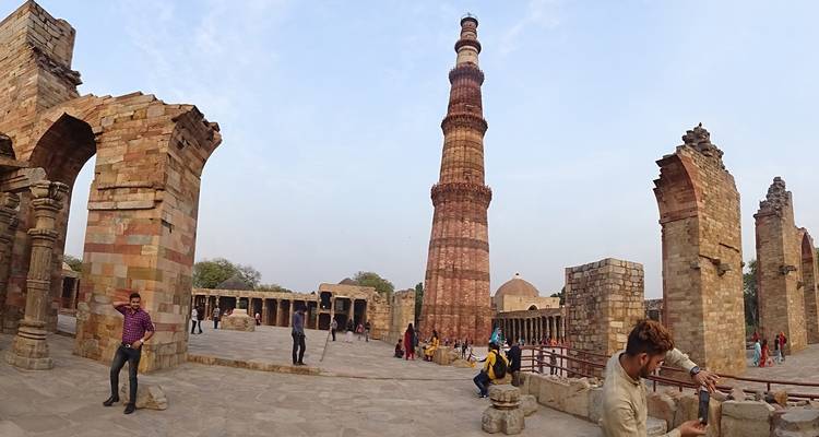 Qutub Minar met bezoekers en ruïnes op de achtergrond.