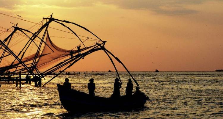 Silhouet van mensen in een boot met grote visnetten bij zonsondergang.