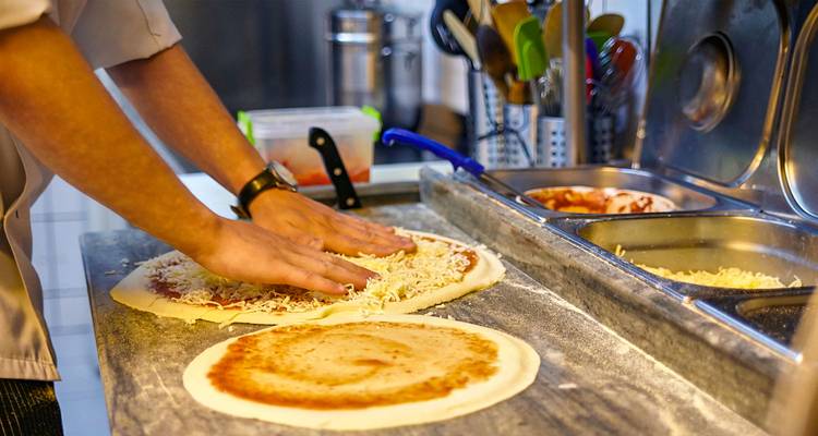 Persona preparando masa de pizza con queso sobre una encimera.
