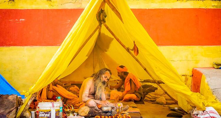 Dos sadhus sentados en una carpa amarilla con humo y ofrendas.