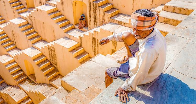 Persona sentada en los escalones de un pozo escalonado antiguo.