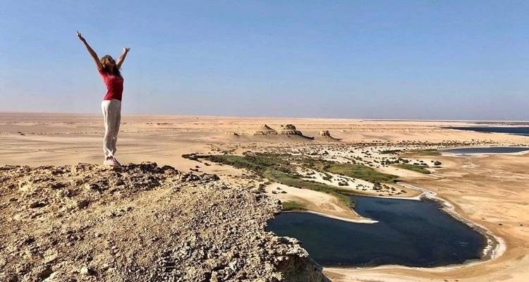 Personne debout sur une falaise rocheuse surplombant le désert et l'eau.
