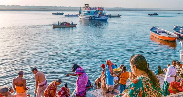 Personas junto al río durante la mañana, con botes y un ferry en el agua.