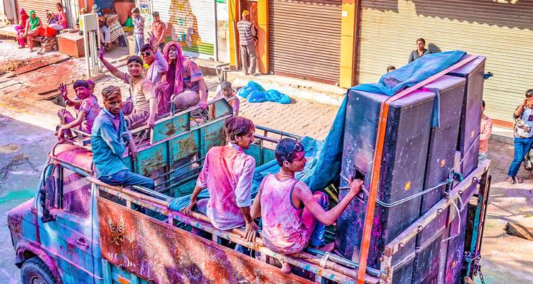 Grupo de personas en un camión cubiertas de polvo de colores durante el festival Holi.