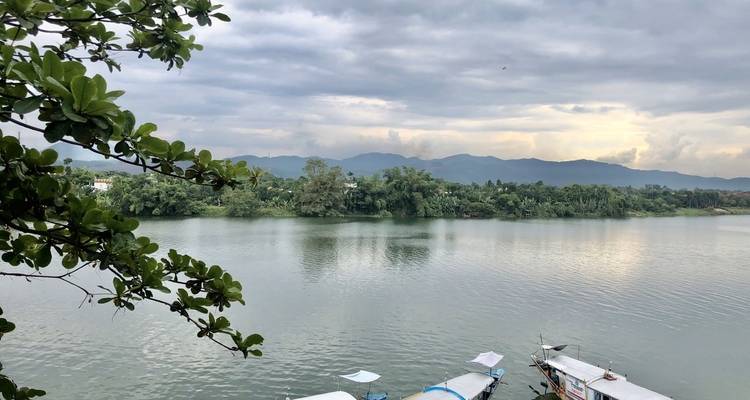 Río tranquilo con botes y árboles verdes exuberantes bajo un cielo nublado.