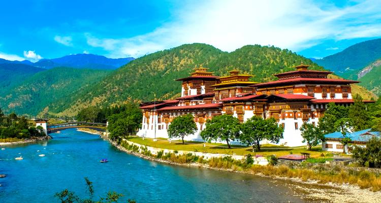 Dzong de Punakha avec montagnes et rivière sous un ciel bleu.