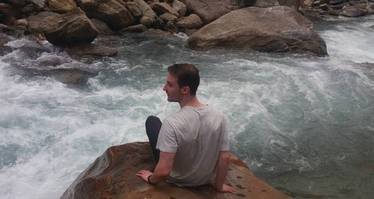 Person, die an einem schnell fließenden Fluss mit großen Felsen sitzt.