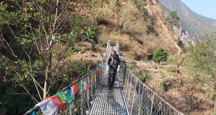 Person, die eine Hängebrücke mit Gebetsflaggen überquert.