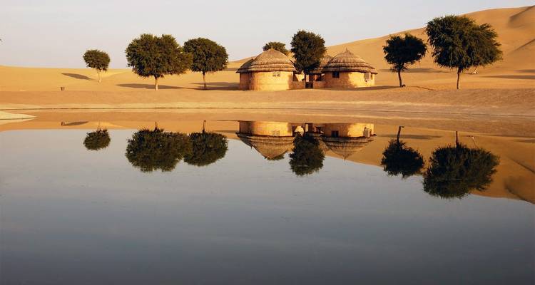 Spiegelnder Wüstenteich mit traditionellen Hütten und Bäumen.