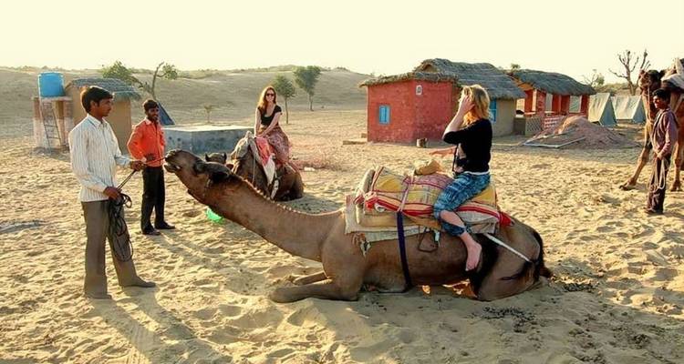 Touristen auf einer Kamelsafari in einer Wüstenlandschaft.