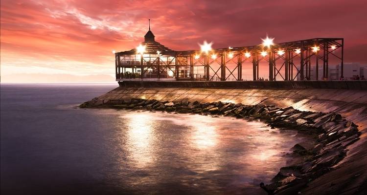 Coastal promenade with a pavilion under a vibrant sunset sky.