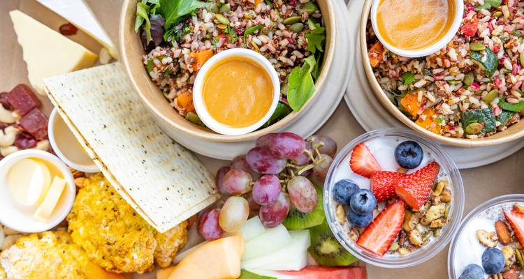Colorida comida gourmet de picnic con ensaladas, fruta, queso y galletas saladas.