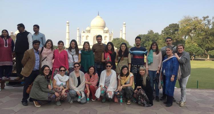 Eine Reisegruppe von Reisenden lächelt zusammen für ein Foto auf der Terrasse des Taj Mahal mit dem Marmormausoleum hinter ihnen.