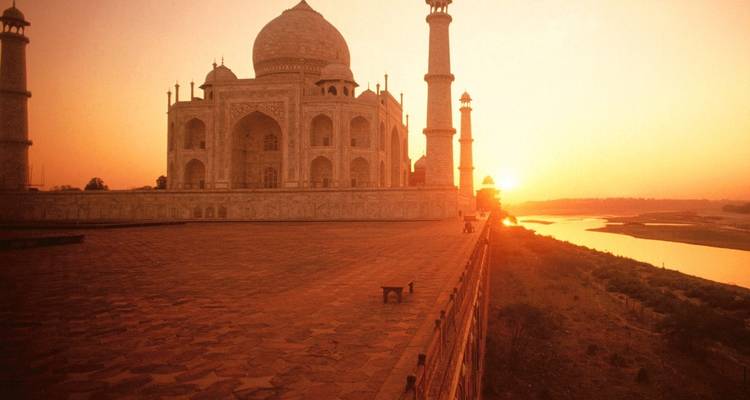 Das Taj Mahal leuchtet bei Sonnenuntergang golden neben dem Yamuna-Fluss, während ein kleines Boot auf dem spiegelnden Wasser dahintreibt.
