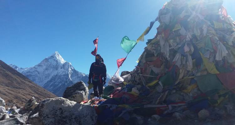 Person, die neben bunten Gebetsfahnen steht, mit Bergen im Hintergrund.
