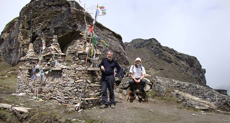 Zwei Männer sitzen neben einer Steinstruktur mit Gebetsfahnen.