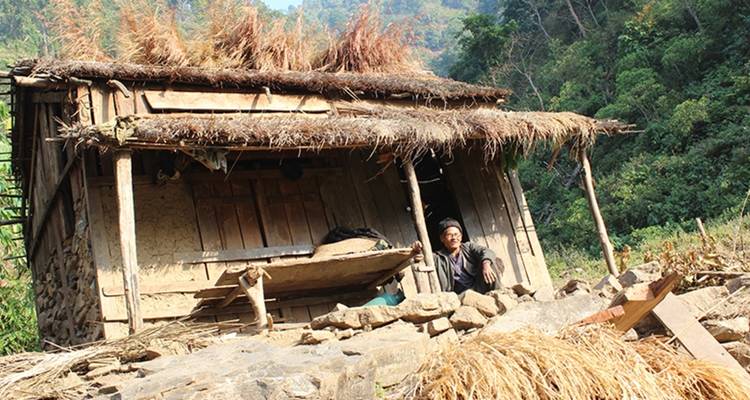 Mann, der vor einem rustikalen strohgedeckten Haus in einer hügeligen Gegend sitzt.