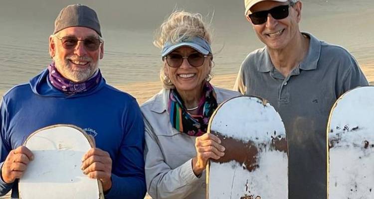 Un grupo de personas sosteniendo tablas de arena, sonriendo a la cámara.