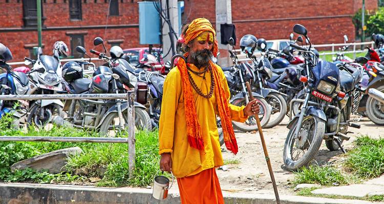 Holy man in robes walking along a line of parked motorbikes.