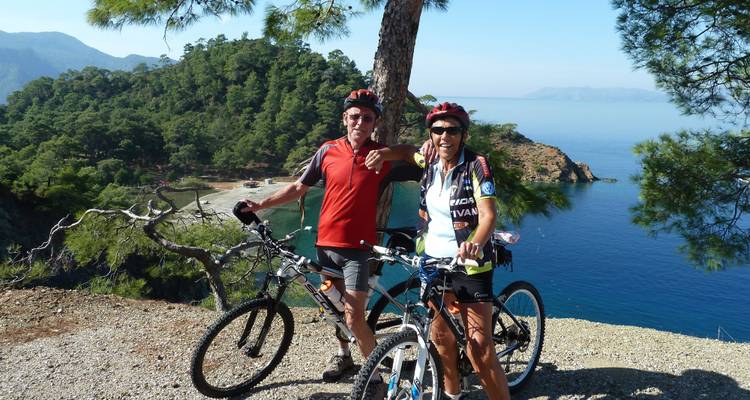Two cyclists with bikes posed on a hill overlooking the sea.