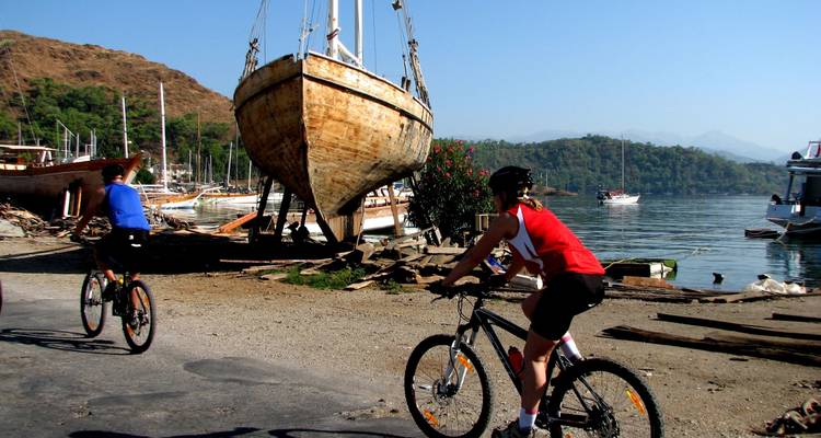 Cyclists riding past a docked ship in a scenic bay.