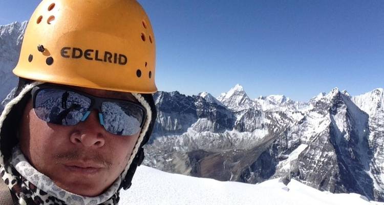 Person mit Helm und Schal auf einem verschneiten Gipfel.