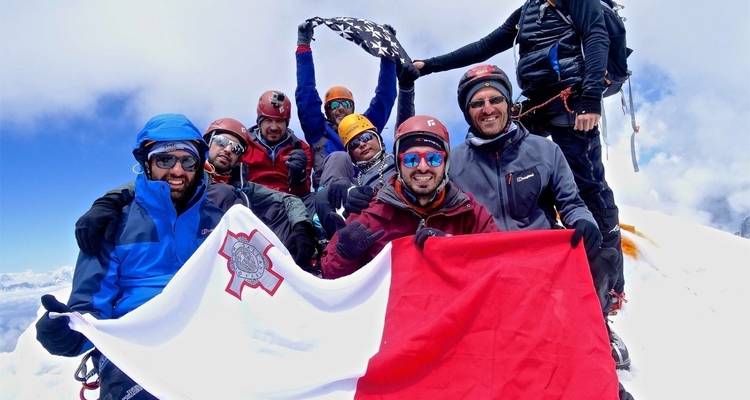 Gruppe von Wanderern, die auf einem schneebedeckten Gipfel mit Fahnen feiern.