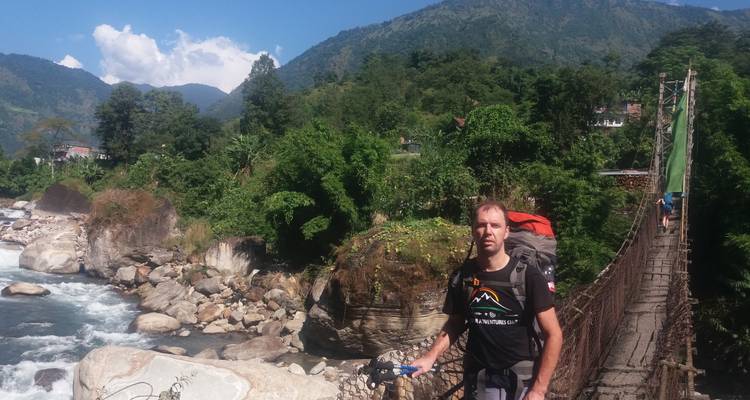 Person, die auf einer Hängebrücke über einem Fluss in einer bergigen Region steht.