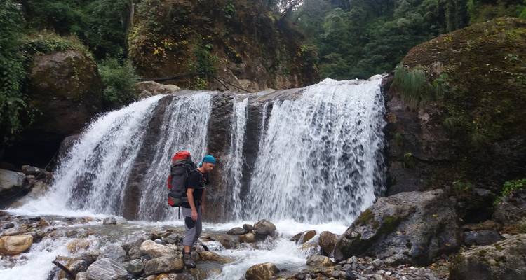 Person, die in der Nähe eines Wasserfalls in einem bewaldeten Gebiet steht.