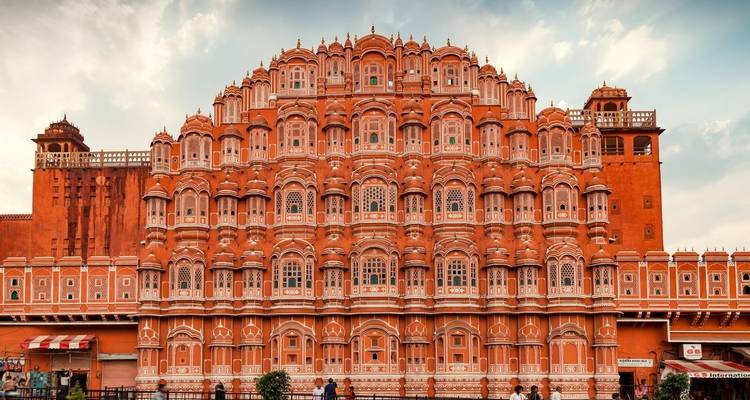 Ein rosafarbenes Schloss mit kunstvollen Fenstern und Menschen darunter.