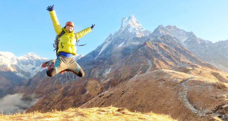 Person jumping in front of snow-capped mountains.
