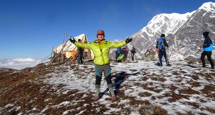 Person standing with open arms near snowy mountains.