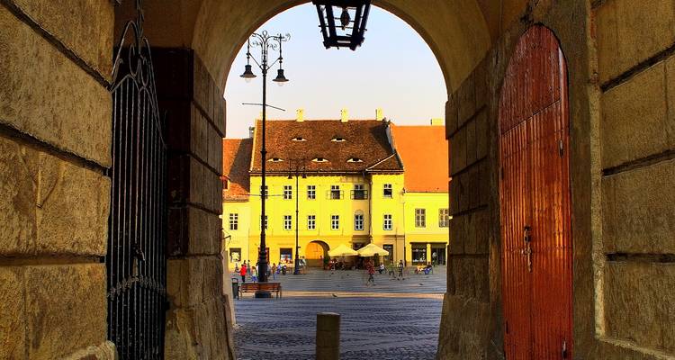 Historic archway framing a sunlit yellow baroque building on Sibiu’s small square