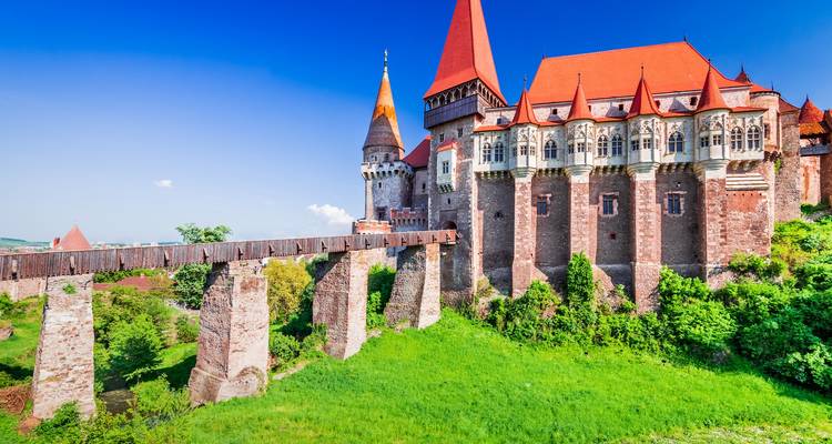 Dramatic Corvin Castle with red roofs and long wooden bridge spanning a green moat