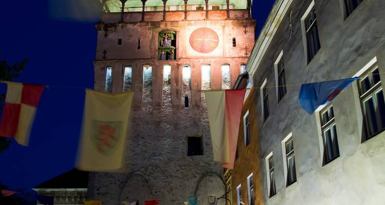 Illuminated medieval clock tower rising above festival flags at night
