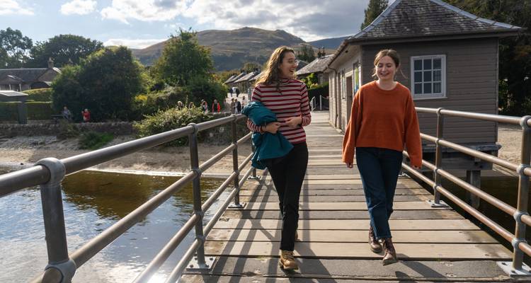 Dos mujeres caminando en un muelle de madera en un pueblo pintoresco junto al agua.