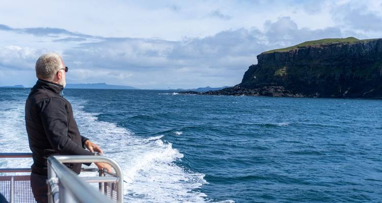 Hombre observando acantilados escarpados desde un barco en un día soleado.