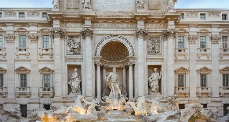 The illuminated statues and Baroque façade of Rome’s Trevi Fountain at dusk.