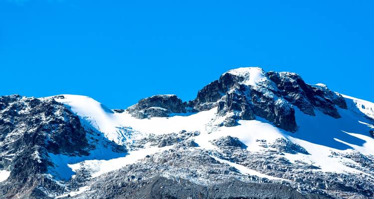 Primer plano de una montaña con cima nevada bajo un cielo azul brillante.