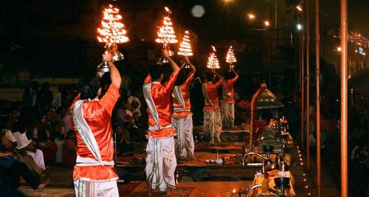 Evening aarti ceremony beside a river with people holding lit lamps.