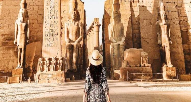 Person, die vor Statuen und dem Eingang eines antiken Tempels steht.