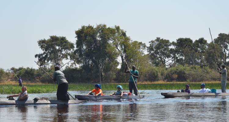 Tourists in mokoros on a river, with trees in the background.