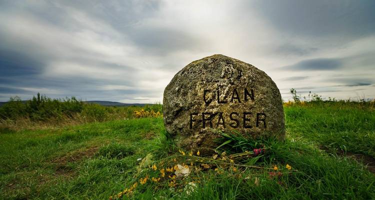 Piedra inscrita con 'Clan Fraser' en un campo cubierto de hierba.