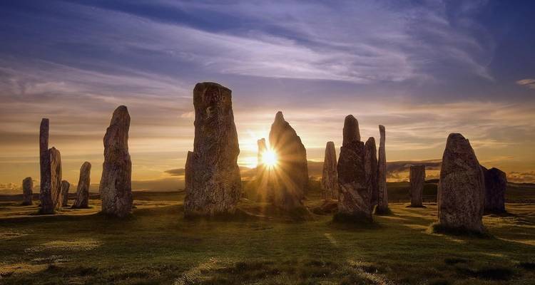 Piedras erguidas con el sol poniéndose detrás de ellas, posiblemente las Piedras de Callanish.