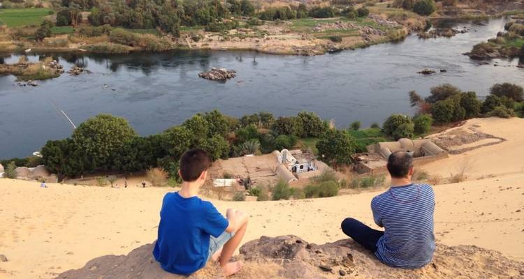 Zwei Menschen sitzen auf einer Sanddüne und blicken auf einen Fluss.